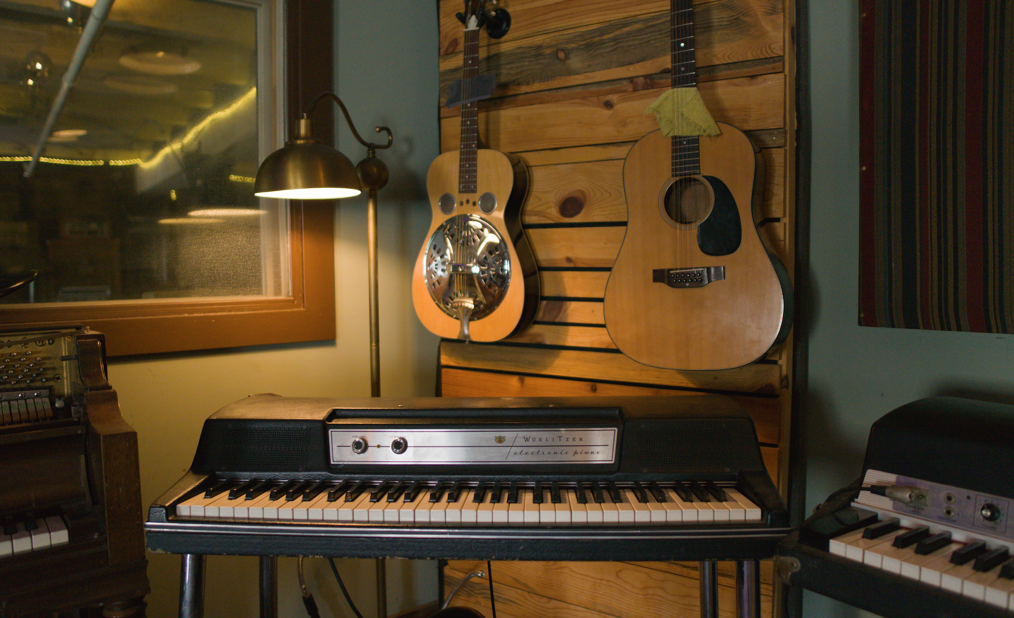 a dobro and an acoustic guitar hanging over a Wurlitzer